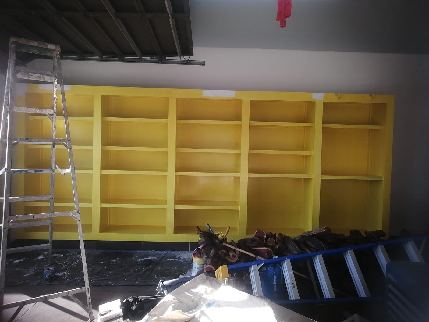 Yellow built-in shelving during finishing work with ladders and tools nearby