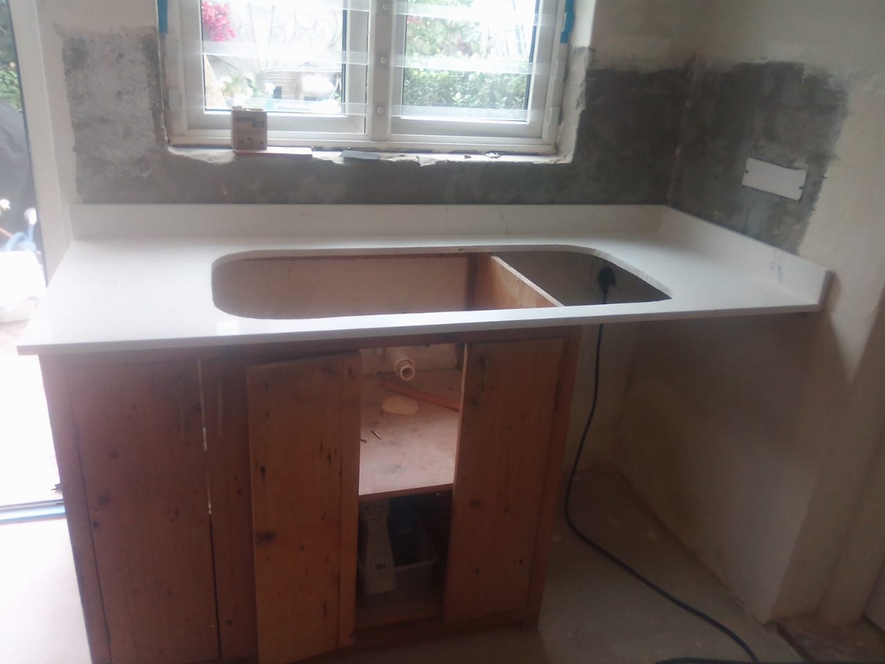 White countertop with a sink opening above timber cupboards during installation