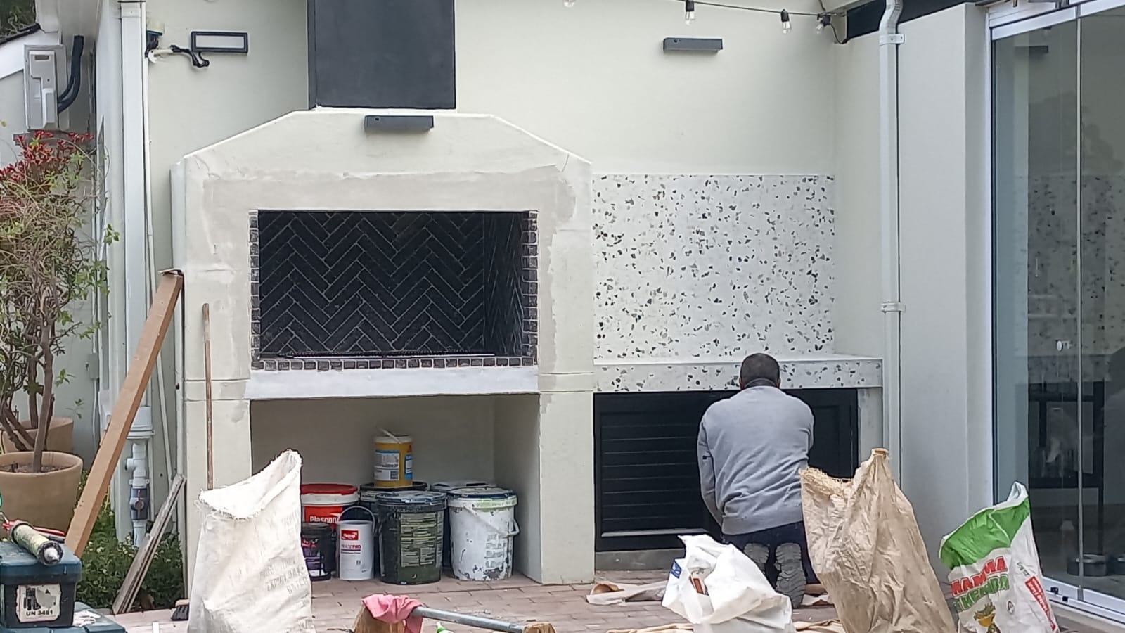 Worker finishing an outdoor braai area with dark herringbone lining and a patterned counter surround