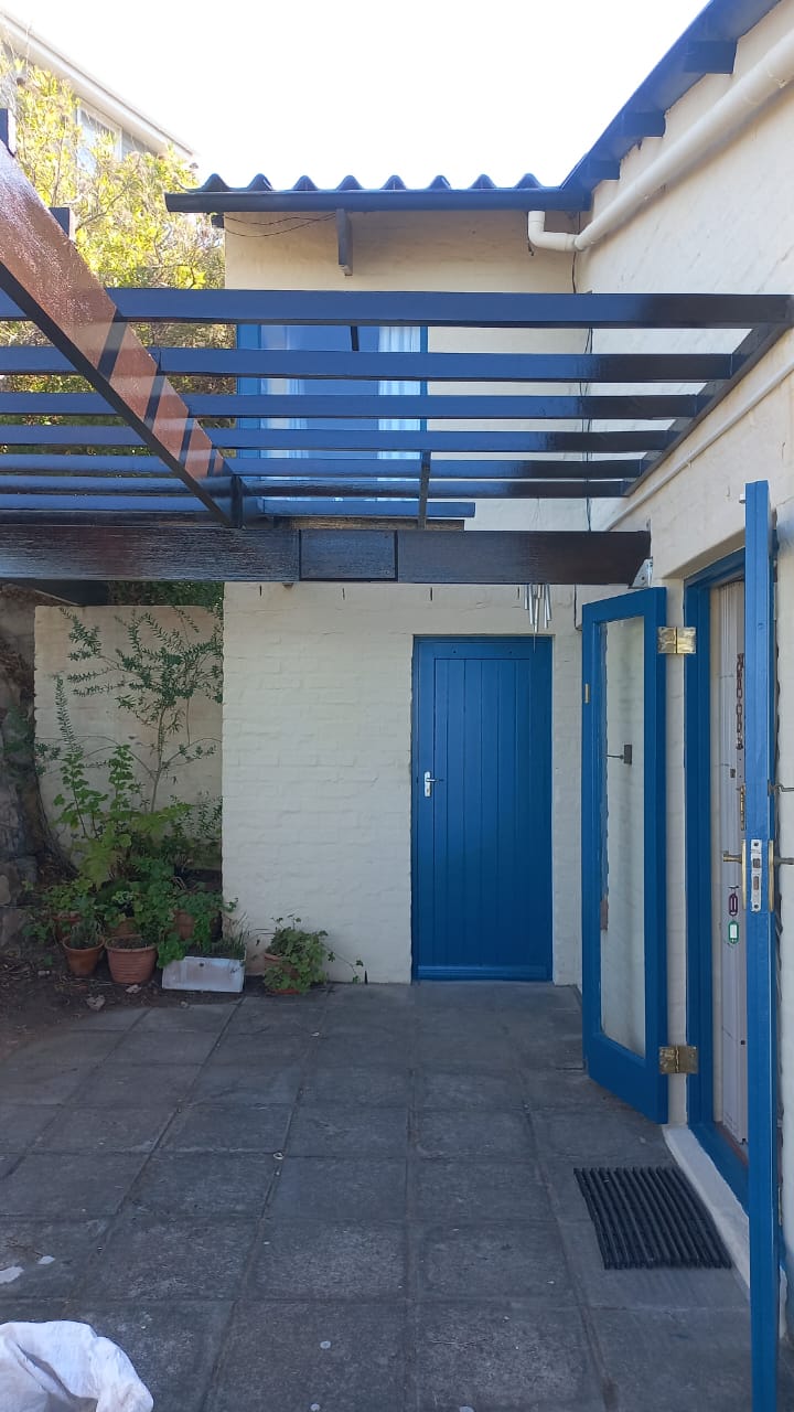 Courtyard with cream walls, blue doors and dark timber pergola beams