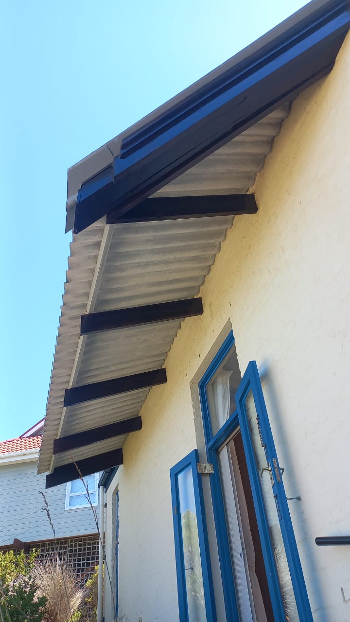 Exterior eaves with dark timber beams above a cream wall and blue window frame