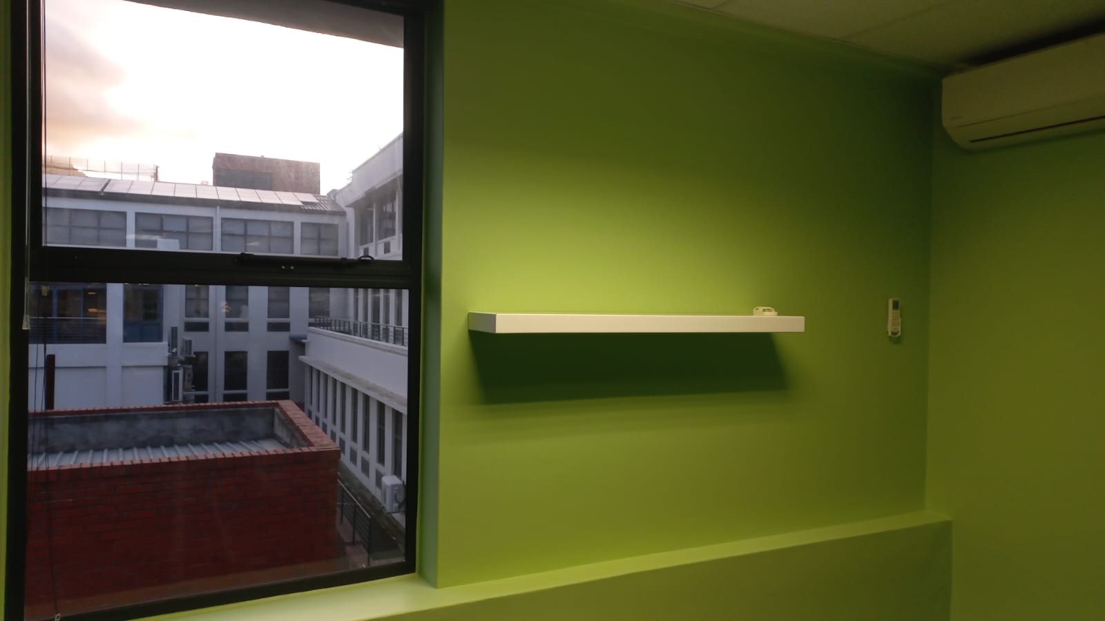 White floating shelf against a green interior feature wall beside a window