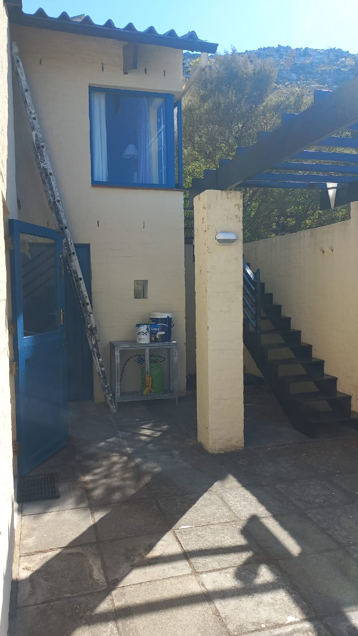 Cream exterior walls, blue window frames and a dark timber staircase with painting equipment nearby