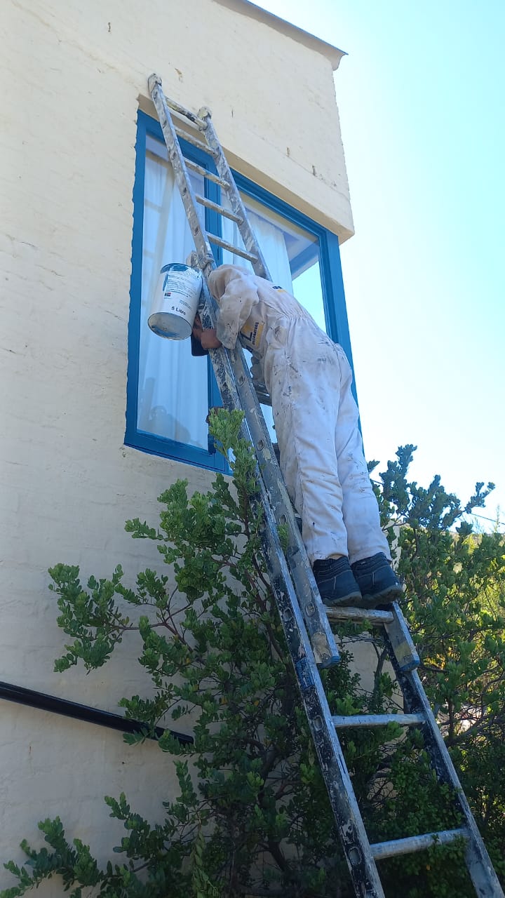 Worker on a ladder painting around a blue exterior window frame
