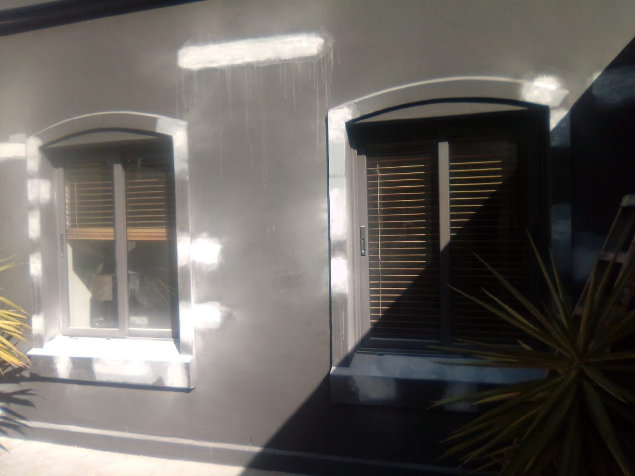 Grey exterior wall with white repair patches around two shuttered windows