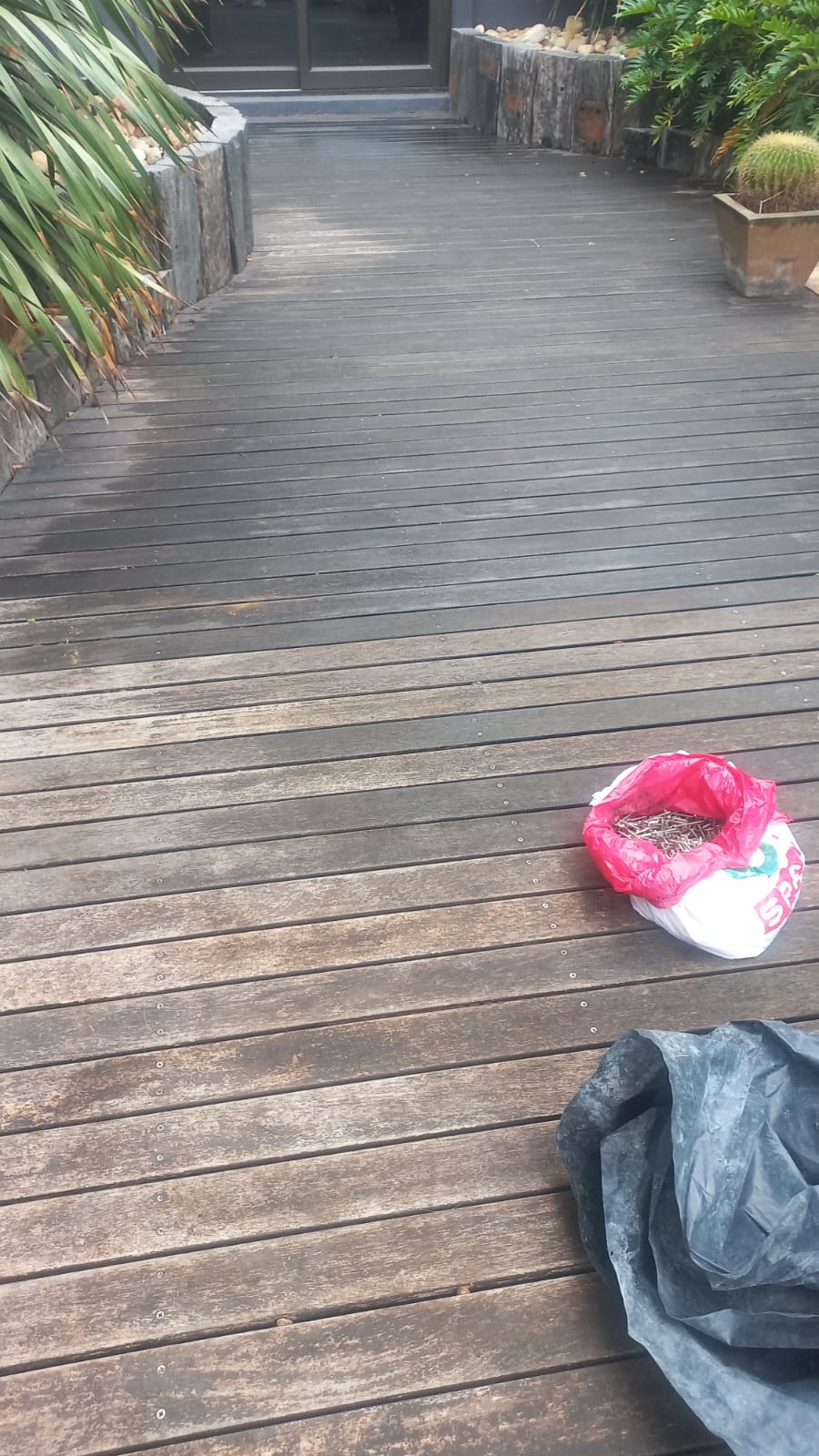Timber deck boards with screws and work materials beside garden beds