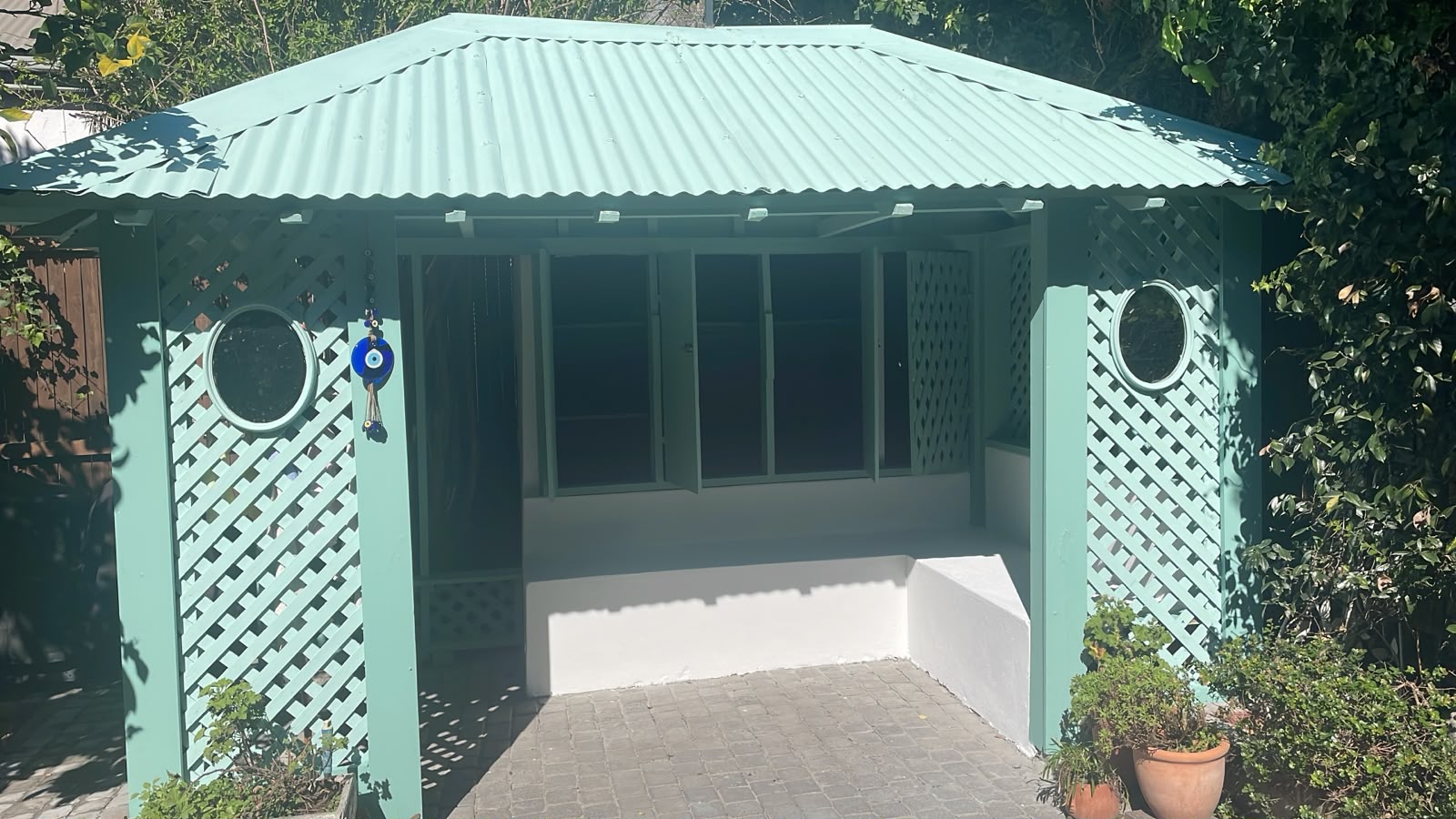 Green painted pool change room with lattice panels, round windows and a paved entrance