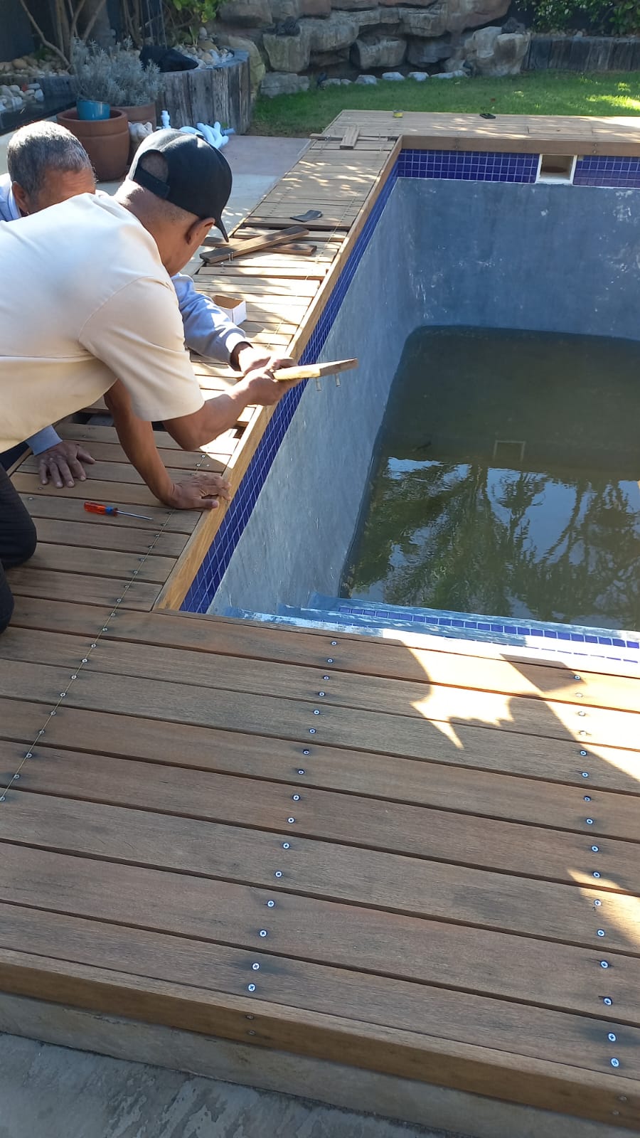 Two workers securing timber deck boards beside a swimming pool
