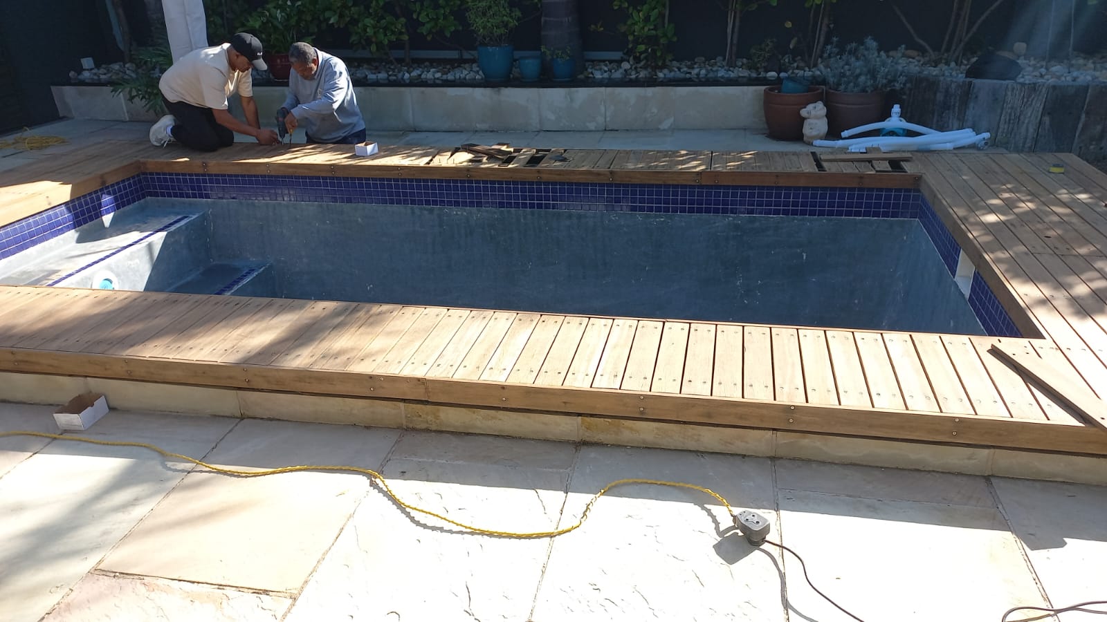 Workers completing timber decking around a drained rectangular pool