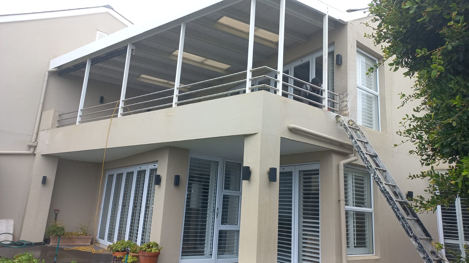 House exterior with a covered upper balcony, metal railings and a ladder during finishing work