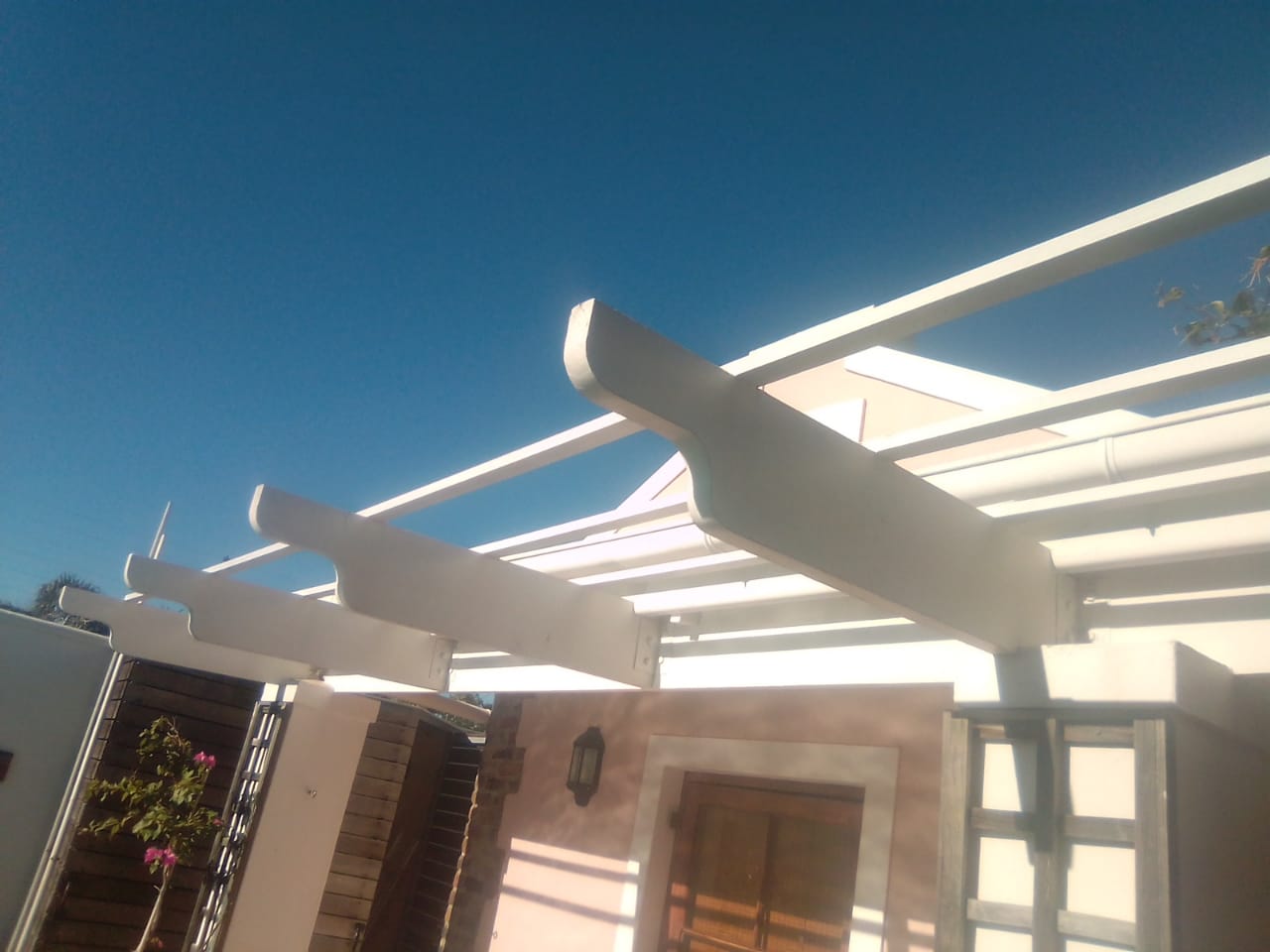 White painted timber patio pergola beams beside a house