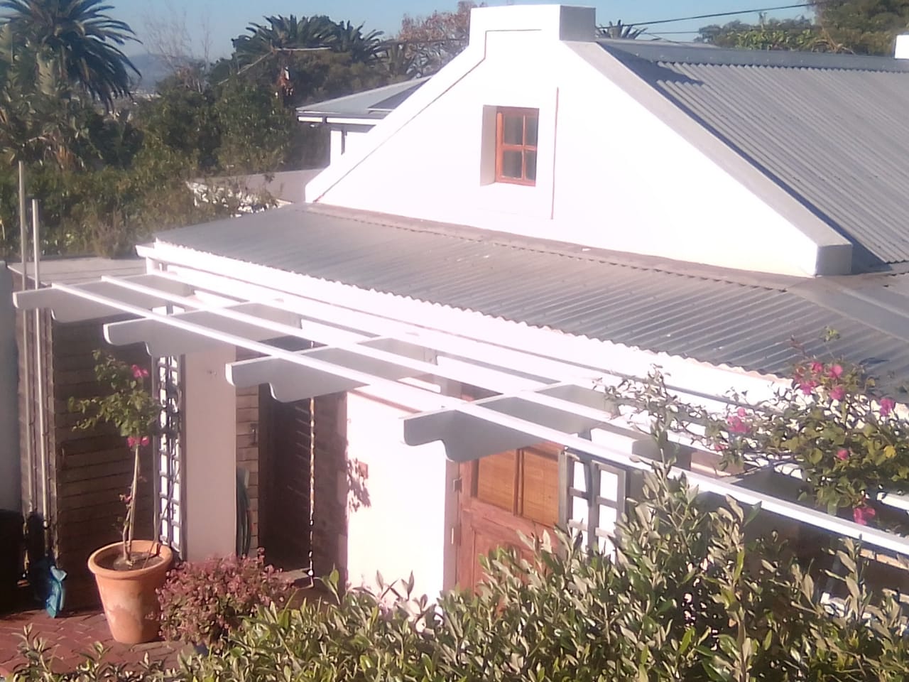 House roof and white painted pergola beams above a garden patio