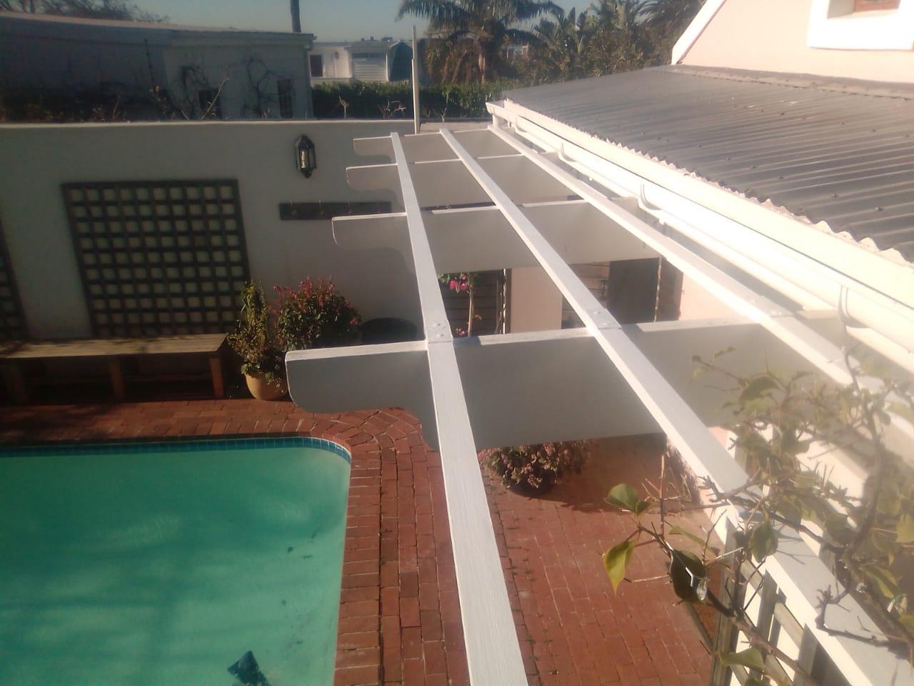 White timber patio framework beside a corrugated roof and swimming pool