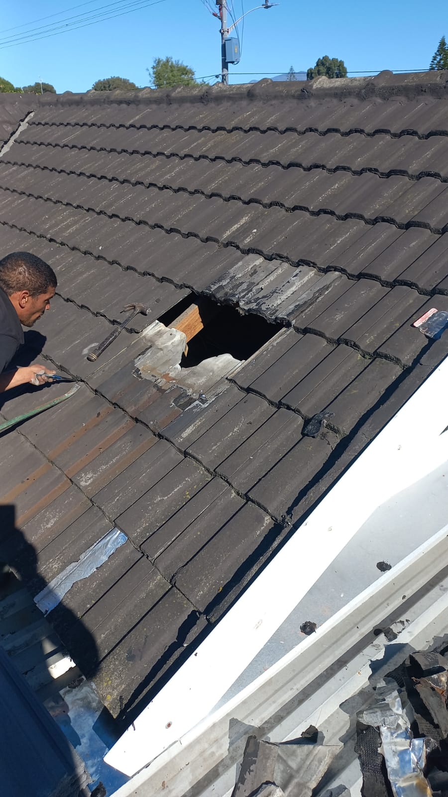 Worker repairing a tiled roof with several tiles lifted around an opening