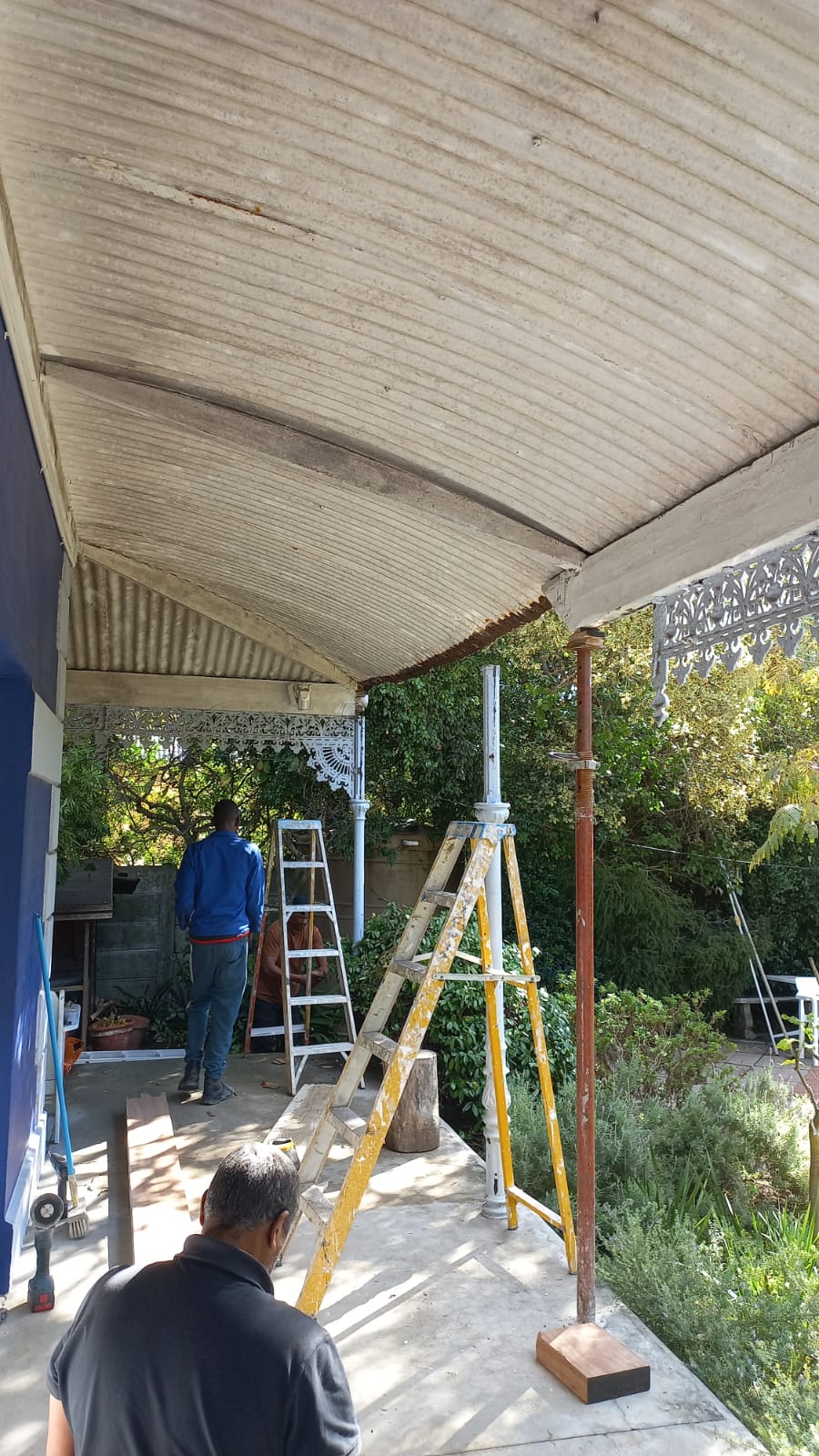 Workers and ladders beneath an older corrugated veranda roof during renovation