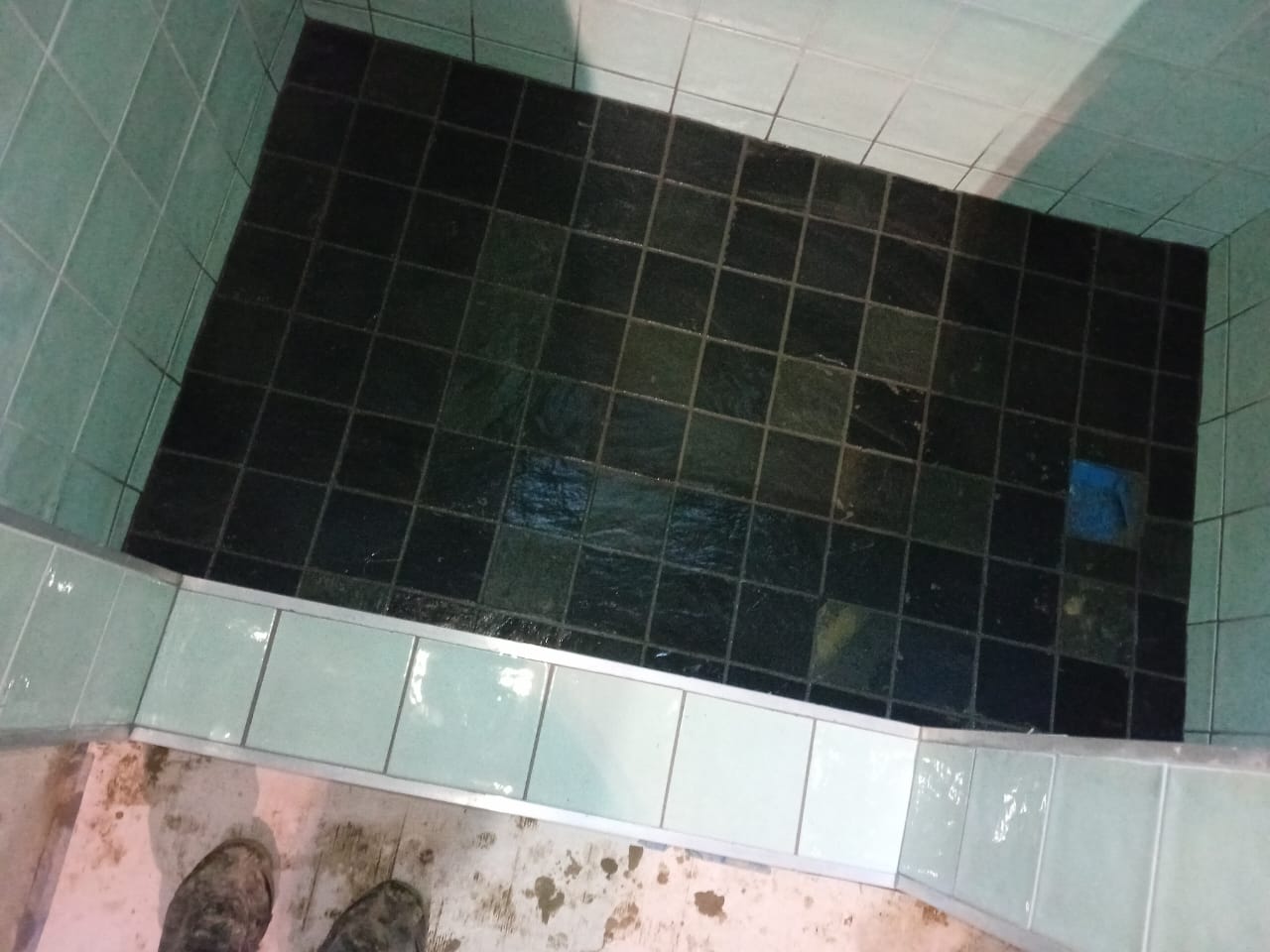 Close view of dark shower floor tiles and a pale tiled threshold during installation