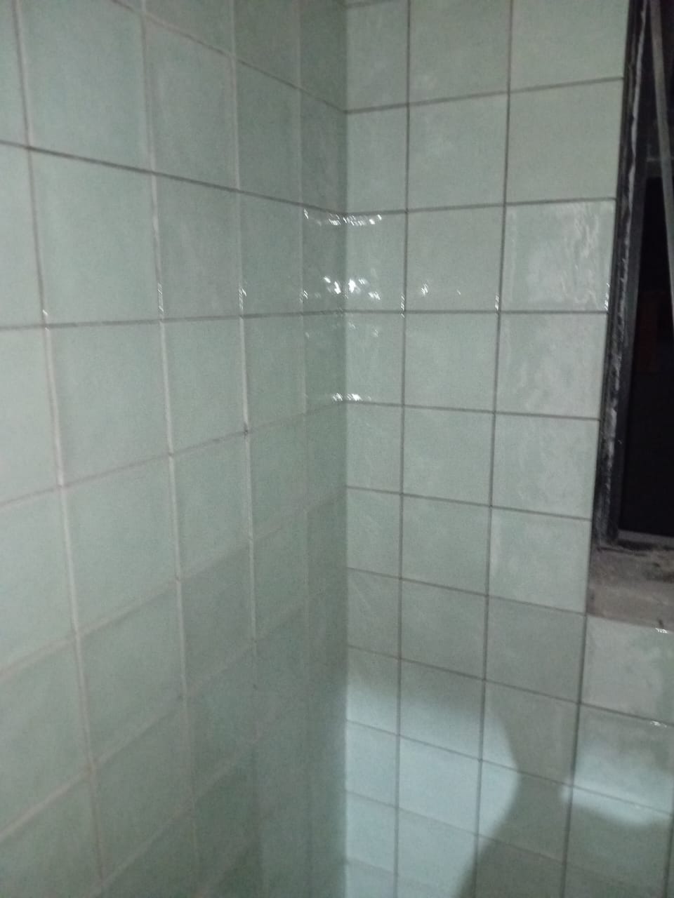 Pale square tiles around a shower corner and window opening