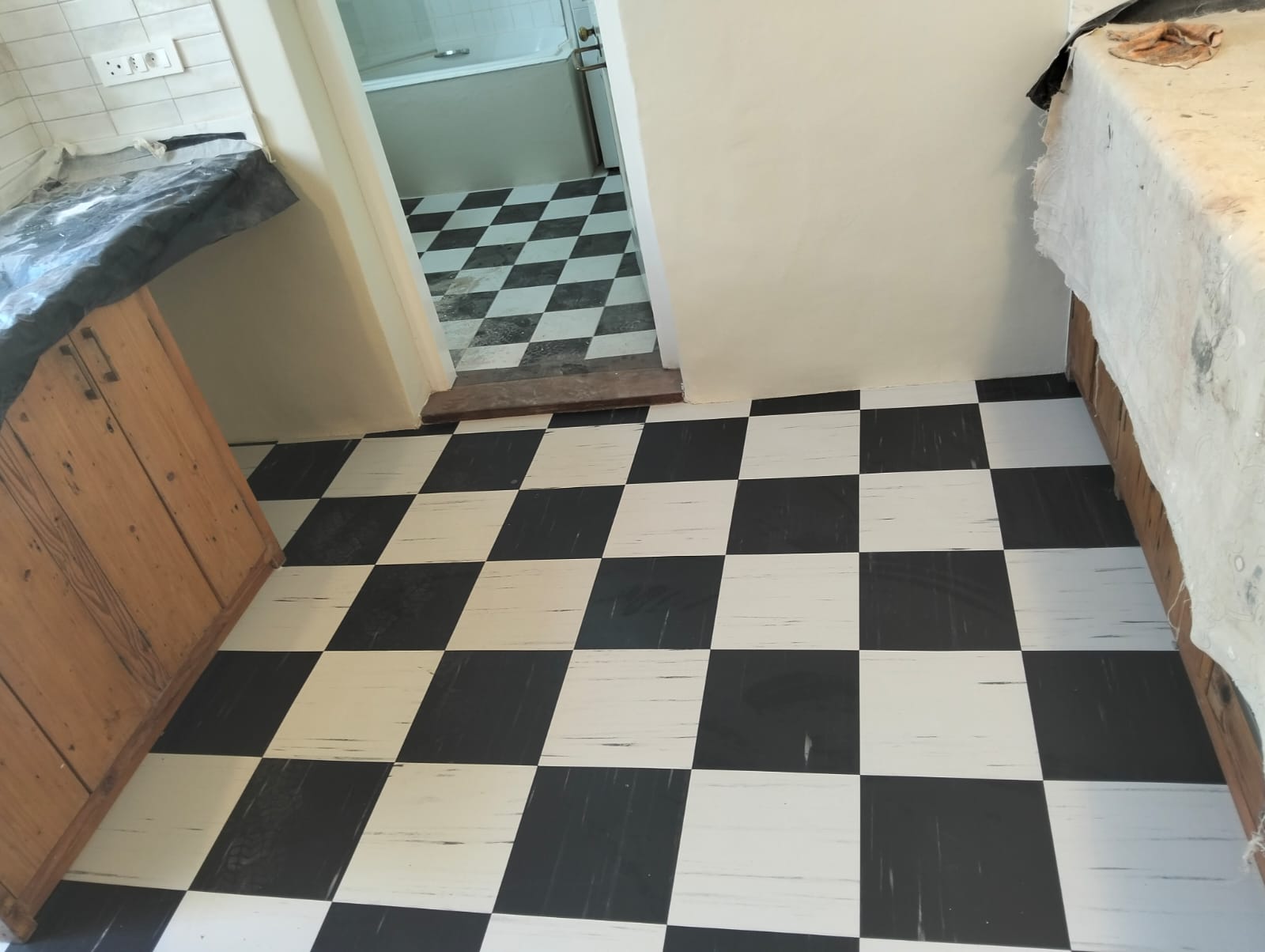 Black-and-white kitchen floor tiles with protected worktops during renovation