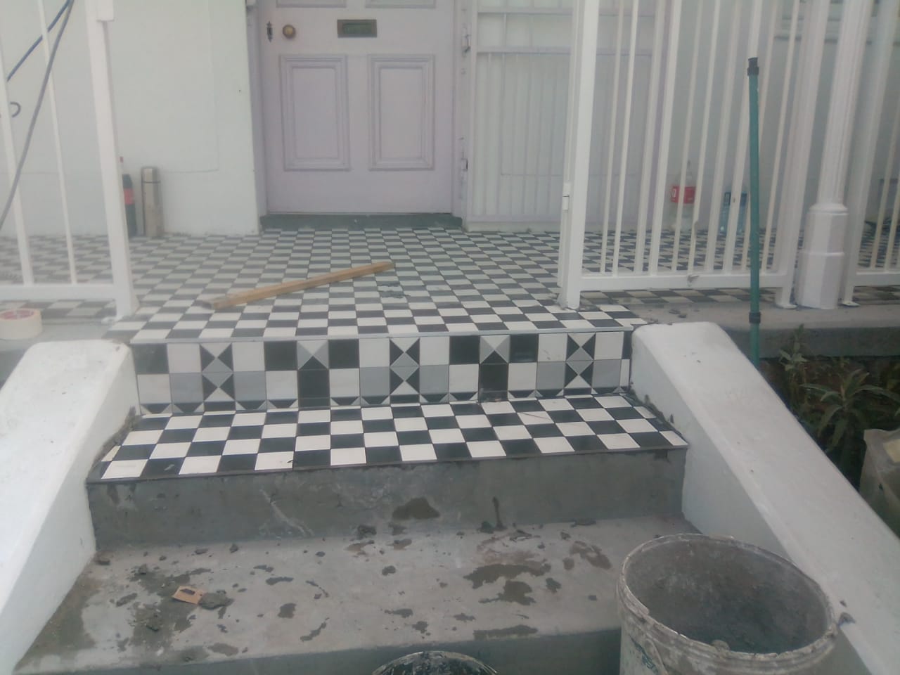 Entrance steps partly tiled in black-and-white patterns with tools and buckets nearby